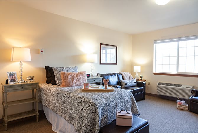 A cozy bedroom featuring a bed with patterned bedding, a leather sofa, lamps, and decor elements.