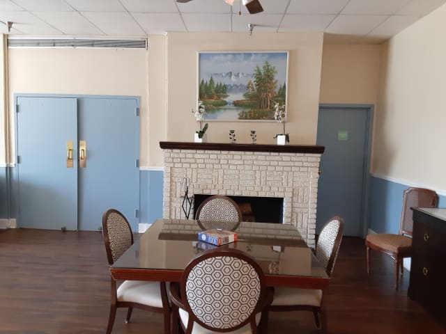 A cozy dining area featuring a table and chairs, with a fireplace decorated with a landscape painting.