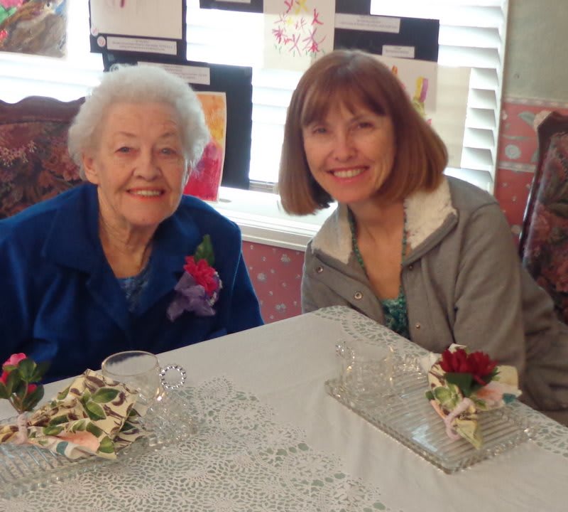 Two women smiling at a table with floral decorations.
