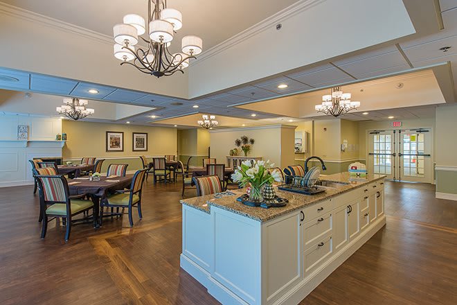 A spacious and elegantly decorated dining area with a central kitchen island, featuring chandeliers and neatly arranged tables and chairs.