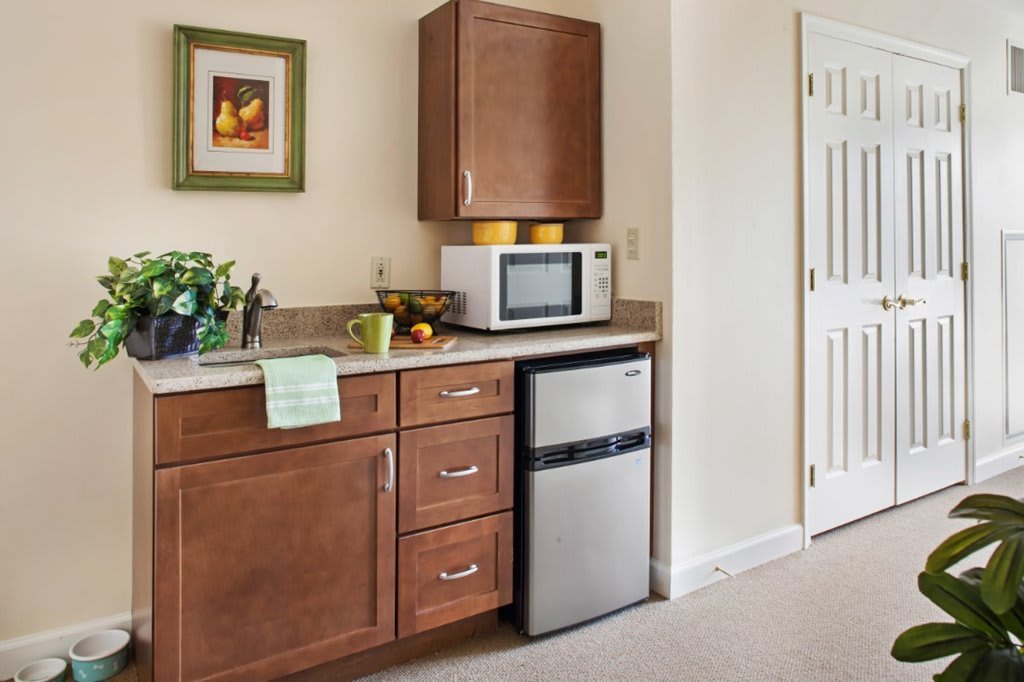 A compact kitchen area with wooden cabinets, a microwave on the counter, and a mini fridge underneath.