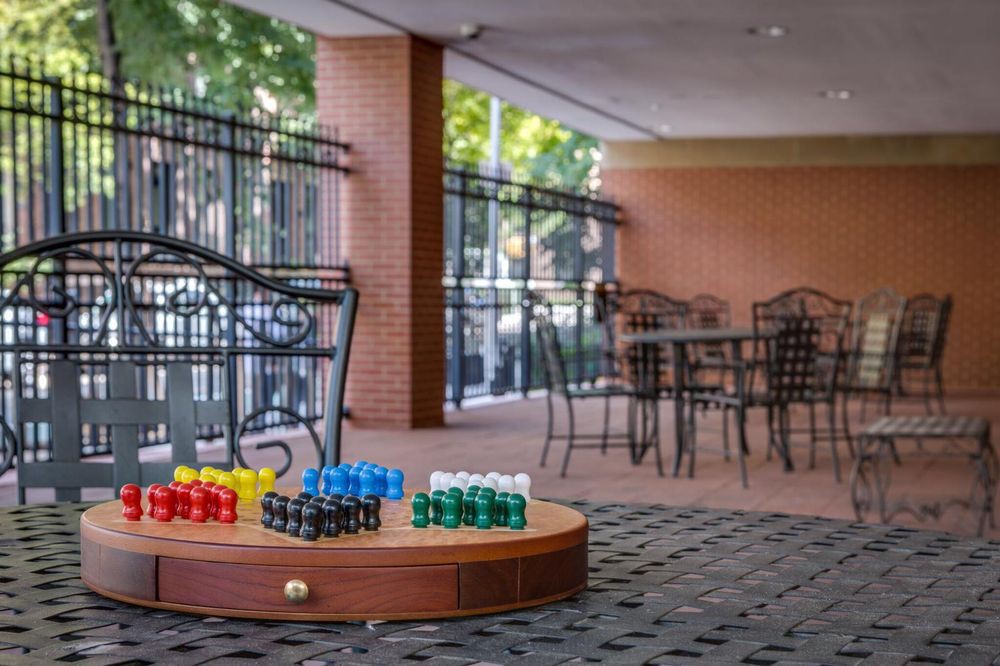 A cozy outdoor patio with colorful jars displayed on a wooden platform, surrounded by chairs and tables under a shaded area with brick walls.