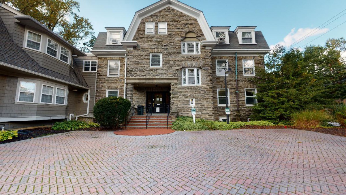 A historic stone building with multiple floors and a welcoming entrance, surrounded by a landscaped area.