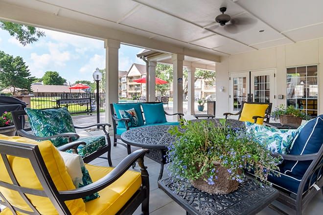 A cozy outdoor patio with colorful cushioned chairs and a table, surrounded by columns and overlooking a scenic view.