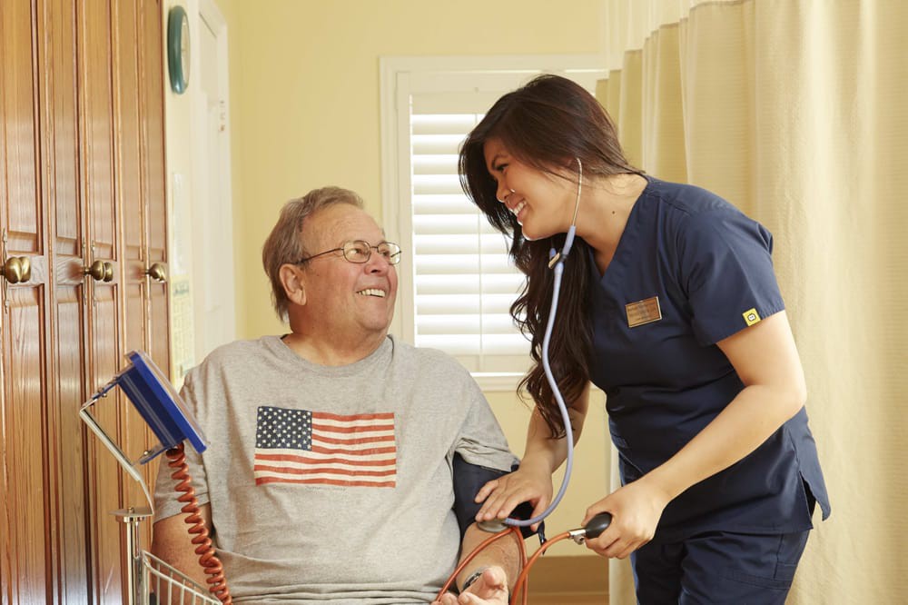 A nurse checks the blood pressure of a smiling patient wearing an American flag t-shirt.