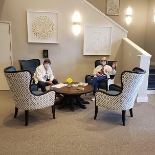 Two people sitting in a lobby lounge area with patterned armchairs and a small table.