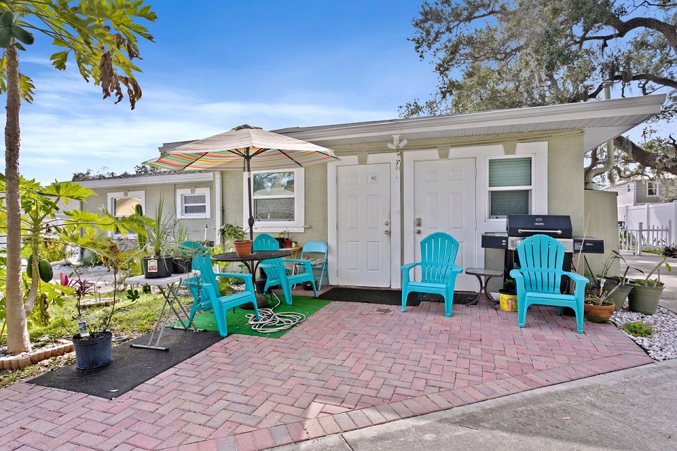 A cozy patio area with turquoise chairs, a table with an umbrella, and a grill.