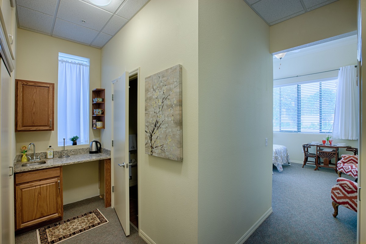 A modern office interior with a minimalist design, featuring artwork on the wall and a small kitchenette area.