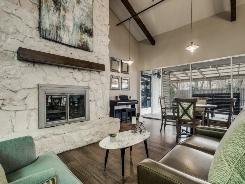 A modern living room featuring a stone fireplace, high ceilings with wood beams, and ample natural light.
