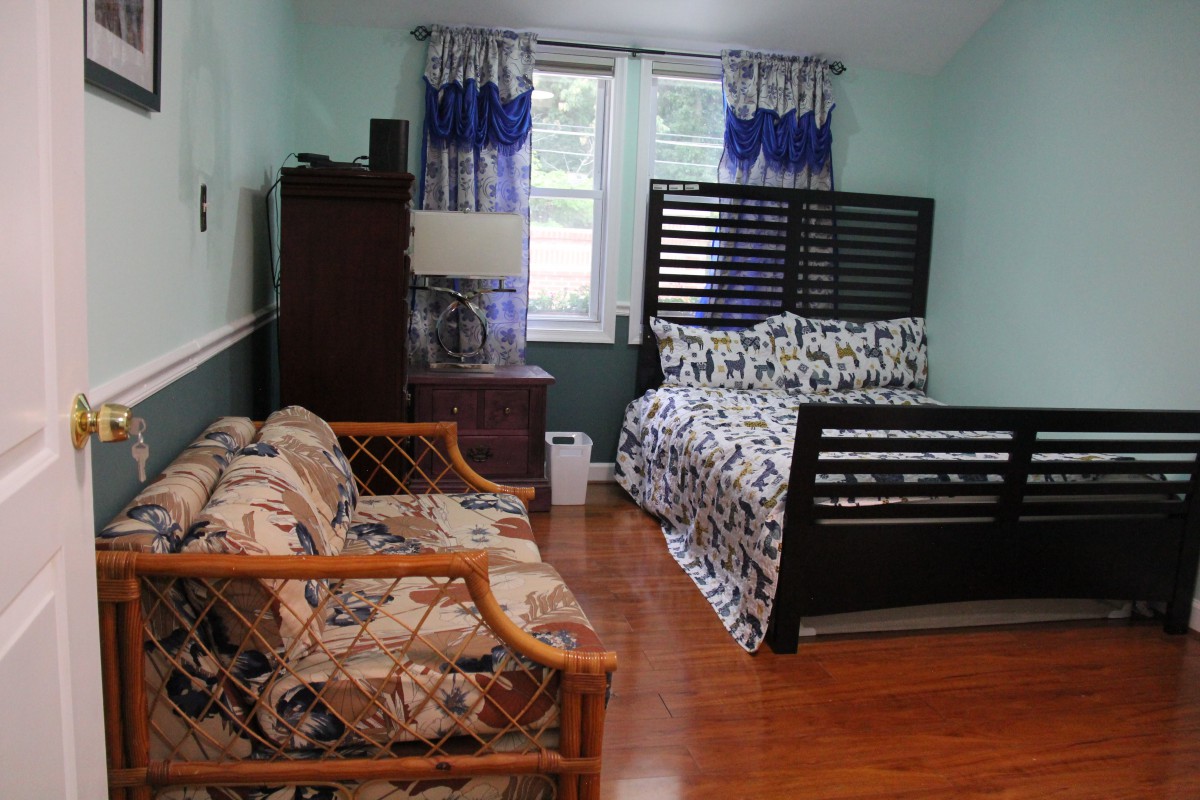 A cozy bedroom with a bed and sofa arrangement, featuring wooden floors and bright curtains.