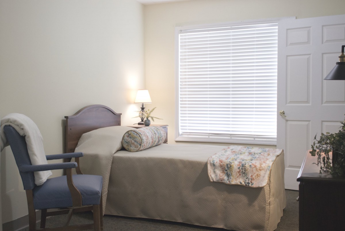 A minimalist bedroom with a single bed, a lamp on the side table, and window blinds.