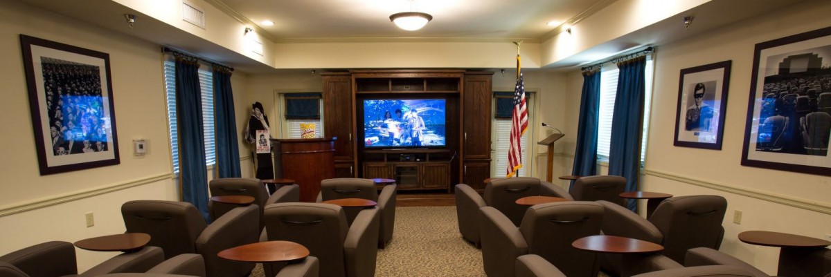 A cozy home theater room featuring comfortable chairs, a large television screen, and a flag in the corner.