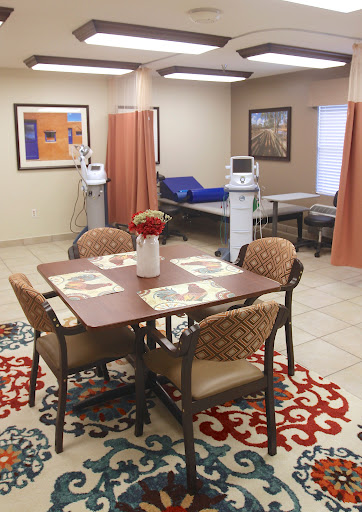 An inviting healthcare space featuring a dining area with chairs, a decorative rug, and patient care stations.