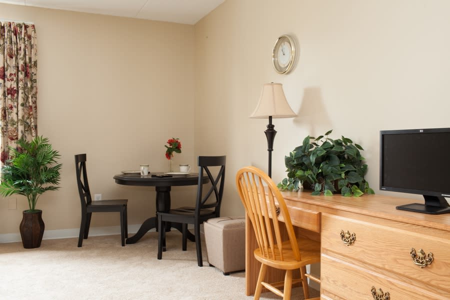 Cozy room corner with a wooden desk, chair, lamp, and small dining table.