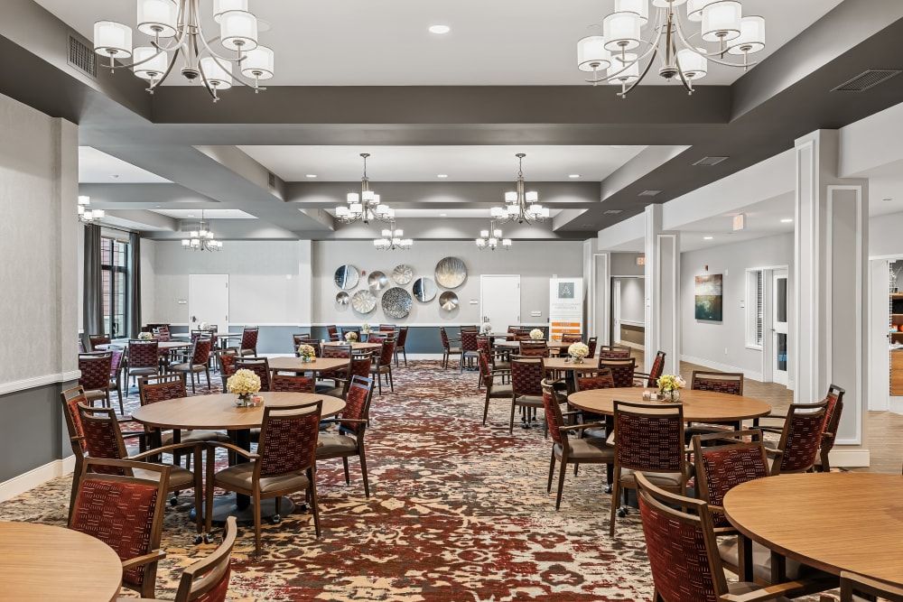 A spacious dining room with elegant chandeliers, neatly arranged tables and chairs, and a richly patterned carpet.