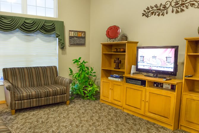A cozy living room with a television and bookshelf, featuring a striped sofa and decorative window drapes.