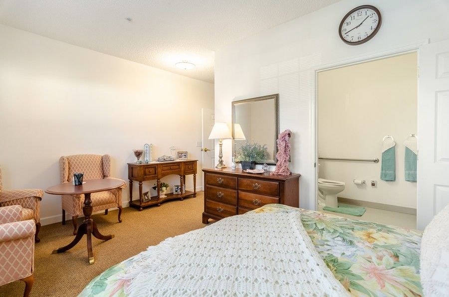 A cozy bedroom with a bed, dresser, mirror, and seating area.