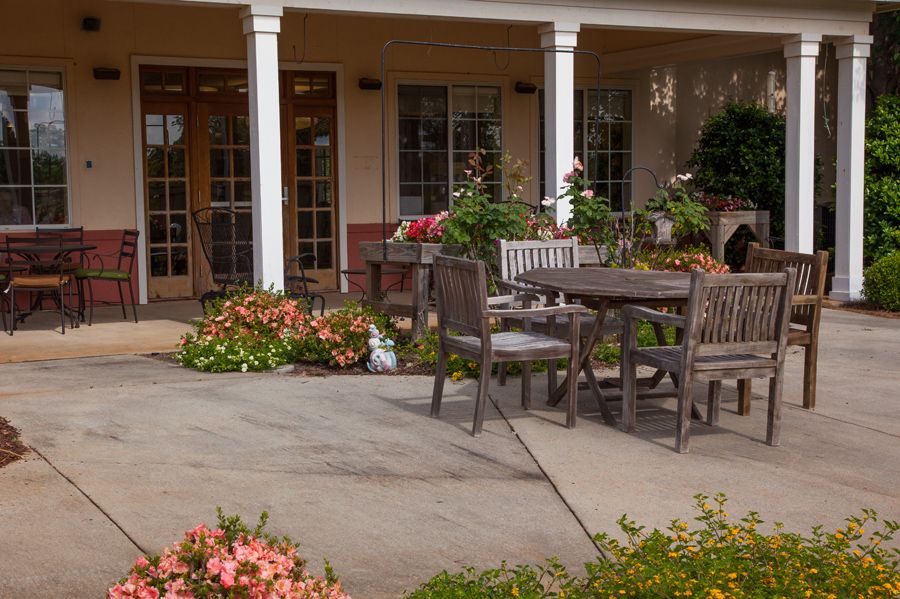 An outdoor patio area with wooden furniture surrounded by blooming flowers and plants.