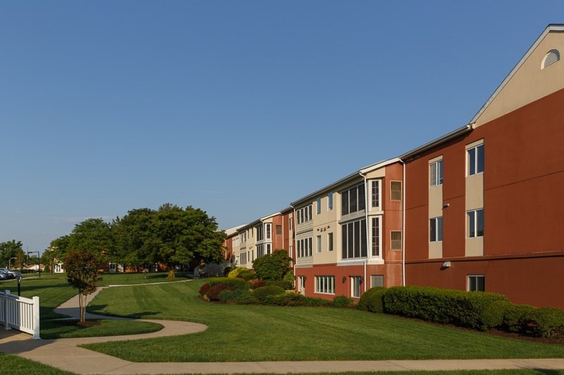 A row of residential apartment buildings with well-maintained lawns and trees under a clear blue sky.
