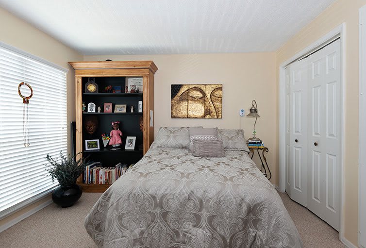 A cozy bedroom with a plush bed, flanked by a wooden bookshelf filled with decor items and books.