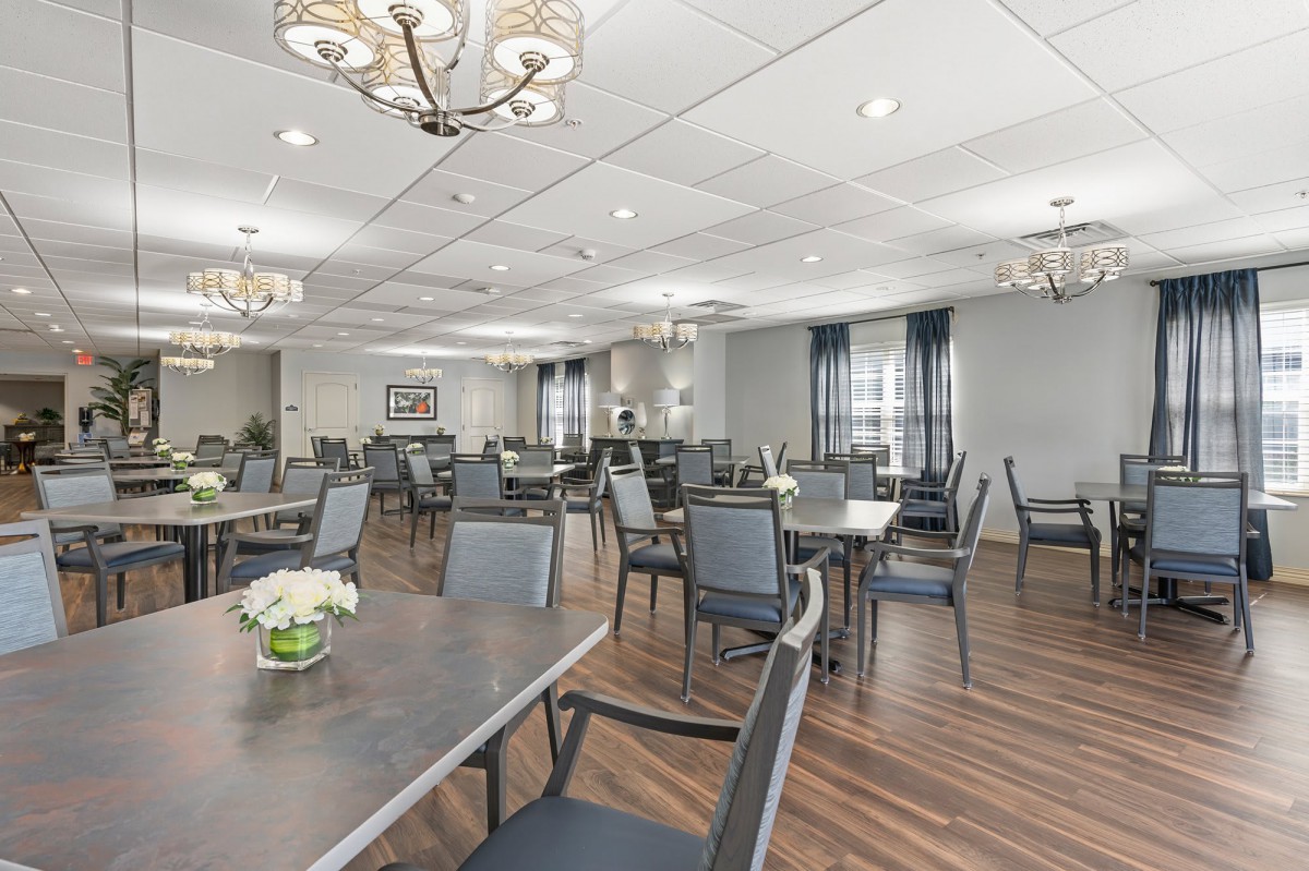 A spacious and elegant dining room with neatly arranged tables and chairs, featuring chandeliers and wooden flooring.