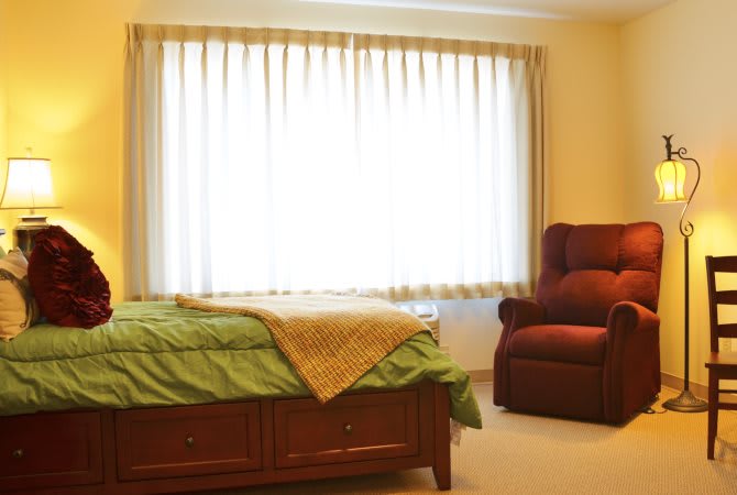 A cozy bedroom with a large window, featuring a bed and a comfortable chair.