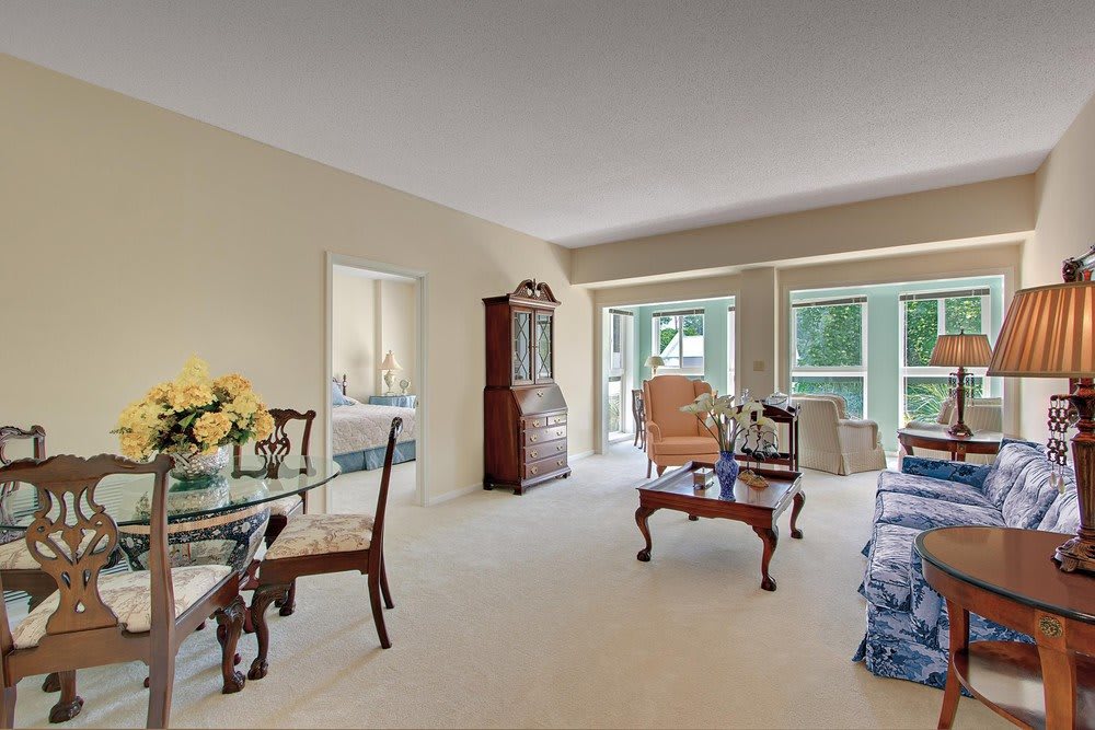 A traditional living room with a dining area, featuring elegant wooden furniture and large windows.
