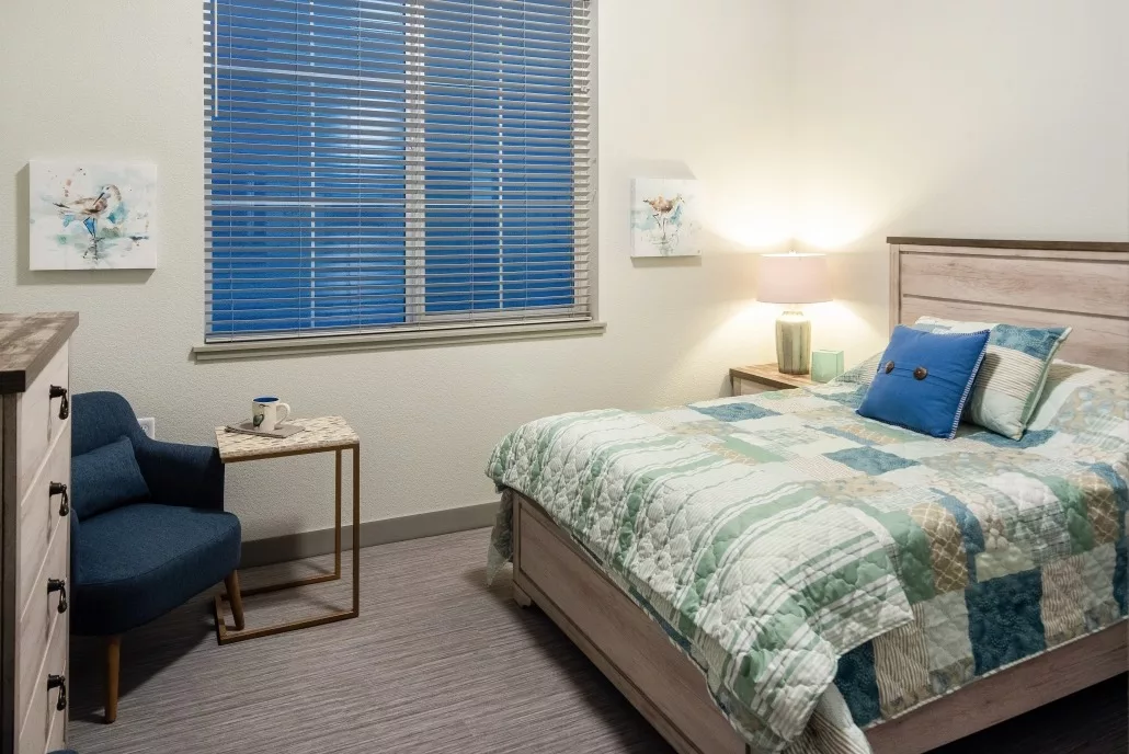 A cozy bedroom with a neatly made bed and a blue chair by the window.