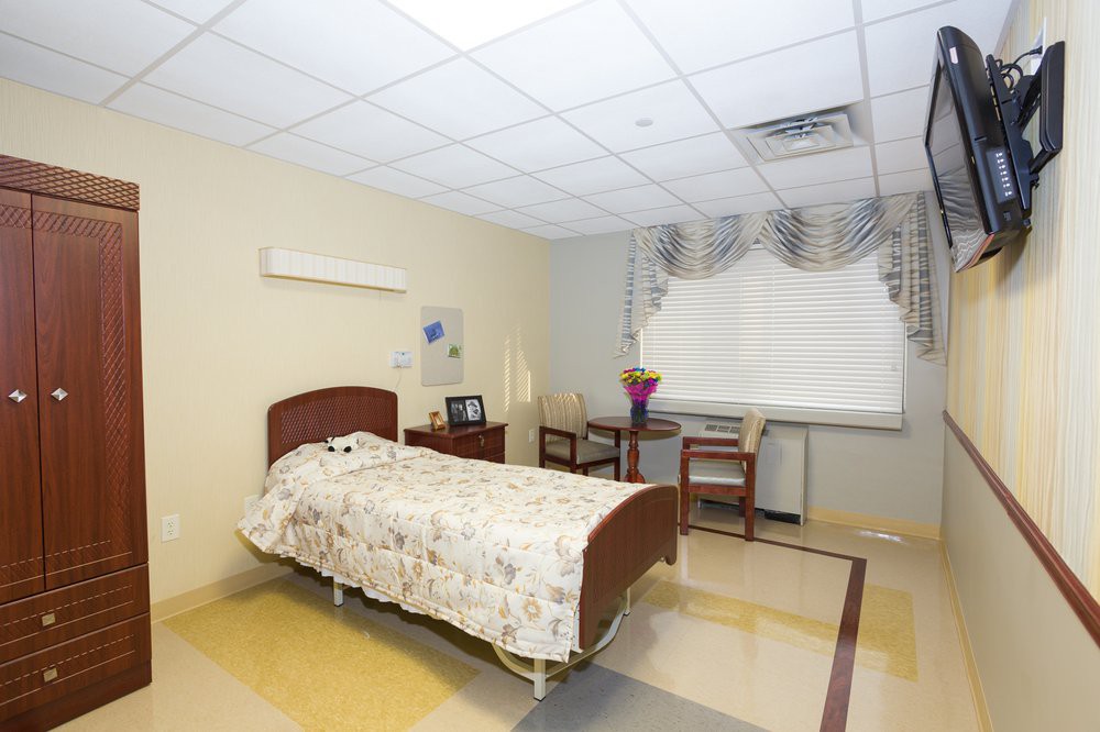 A clean and simple hospital room with a single bed, chairs, and a window with curtains.