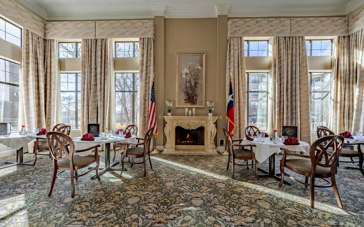 An elegant dining room with large windows, a fireplace, and neatly set tables.