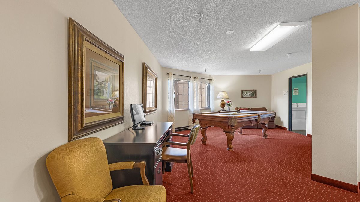 A hotel recreation room featuring a pool table, desk with chairs, and framed artwork on the walls.