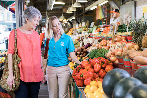 Two women explore the colorful offerings at a vibrant farmers market, discussing fresh vegetables together.