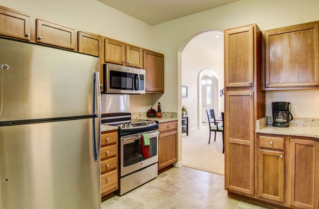 A modern kitchen with wooden cabinets, stainless steel appliances, and an archway leading to the dining area.