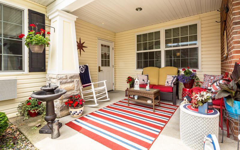 A cozy porch with a red and white striped rug, cushioned seating, a rocking chair, and decorative potted plants.