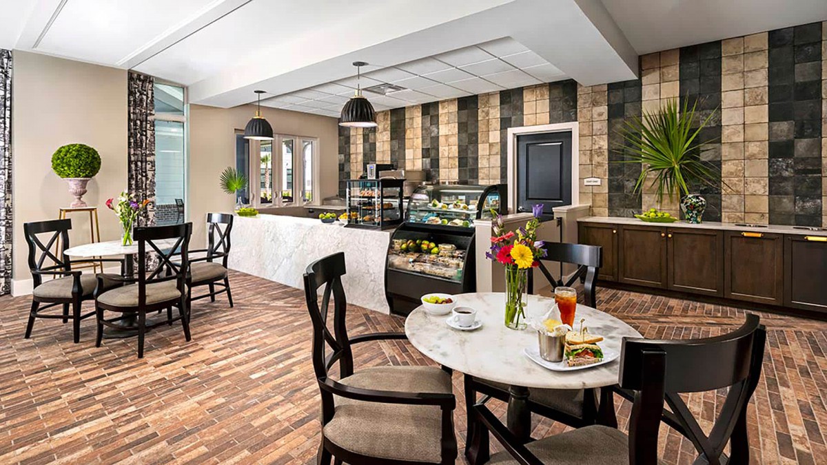 A modern and elegant cafe interior with neatly arranged tables and chairs, featuring a dessert display and floral decorations.
