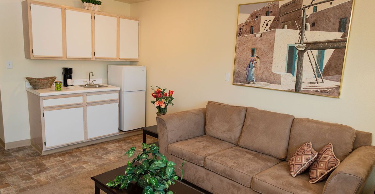 A cozy living area featuring a brown sofa, kitchenette, and wall art.