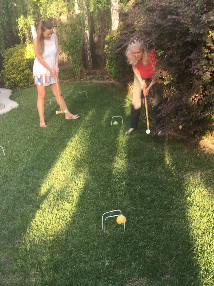 Two people playing croquet on a sunny lawn.