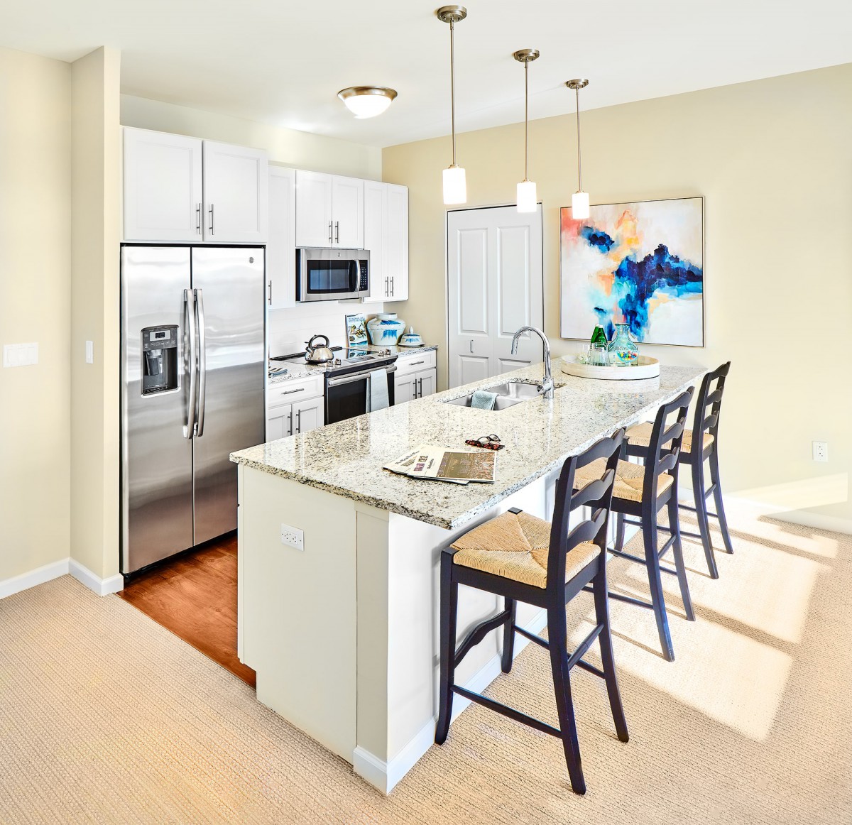 A modern kitchen with stainless steel appliances and a central island featuring bar stools and pendant lighting.