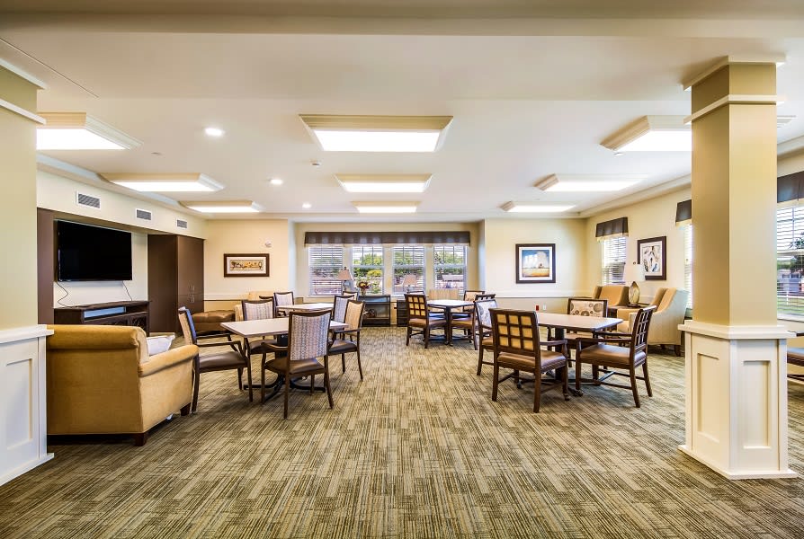 A spacious dining area with tables and chairs, featuring large windows and warm lighting.