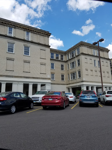 A view of a multi-story hotel building with parked cars in front under a partly cloudy sky.