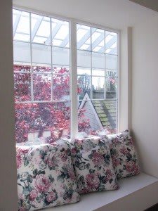A cozy window seat adorned with floral cushions overlooks autumn-colored foliage outside.