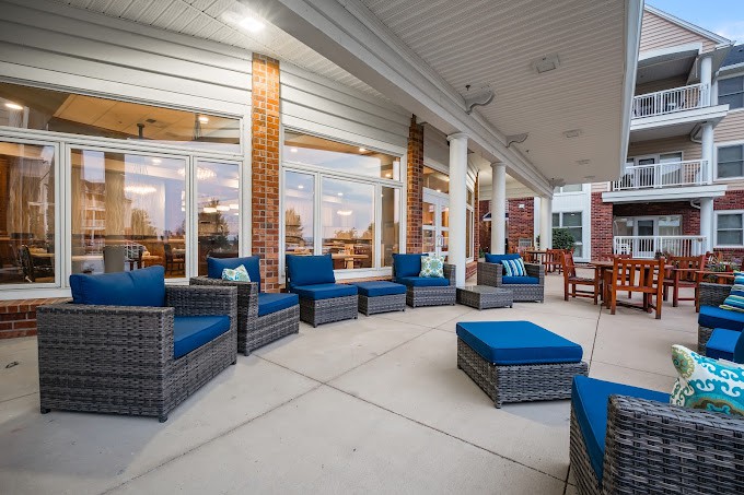 A spacious covered patio with comfortable wicker furniture and blue cushions, set against a brick building.
