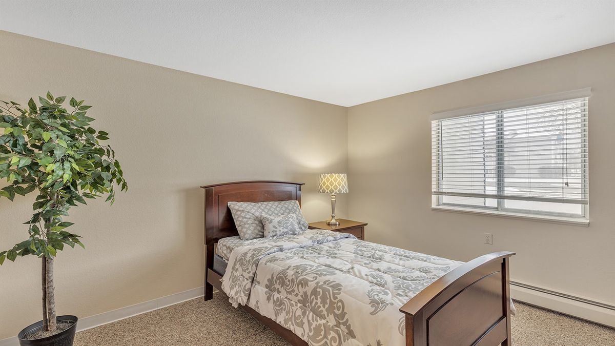 A cozy bedroom with a single bed, lamp, and window with blinds.