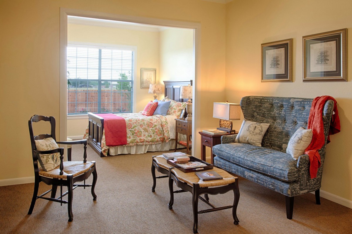 A cozy living area with a sofa and tables connected to a bedroom featuring a bed and large window.
