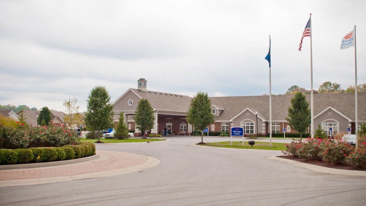 A large building with a driveway, surrounded by trees and a flagpole.