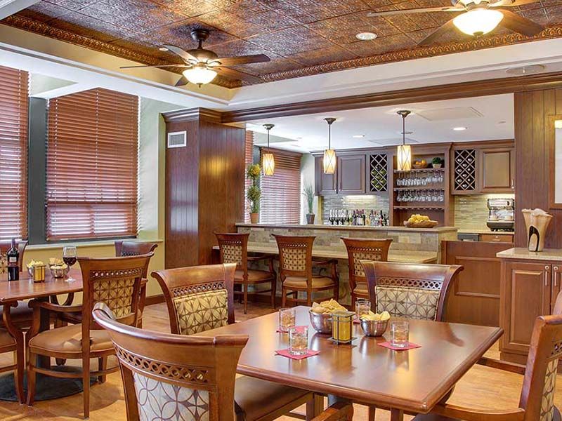 A cozy restaurant interior featuring a dining area with wooden furniture and a bar.