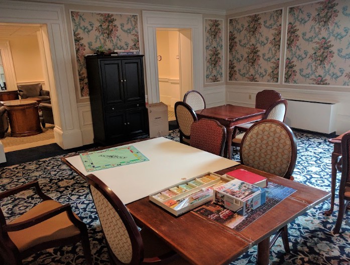 A cozy meeting room with floral wallpaper, a wooden table surrounded by chairs, and various items on the table.
