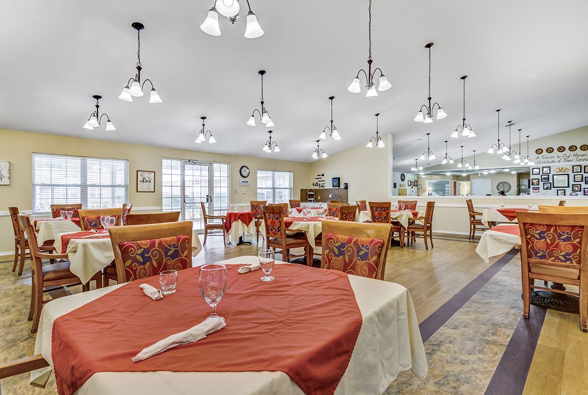 A spacious dining area with neatly arranged tables and chairs, adorned with red and white tablecloths, under warm interior lighting.