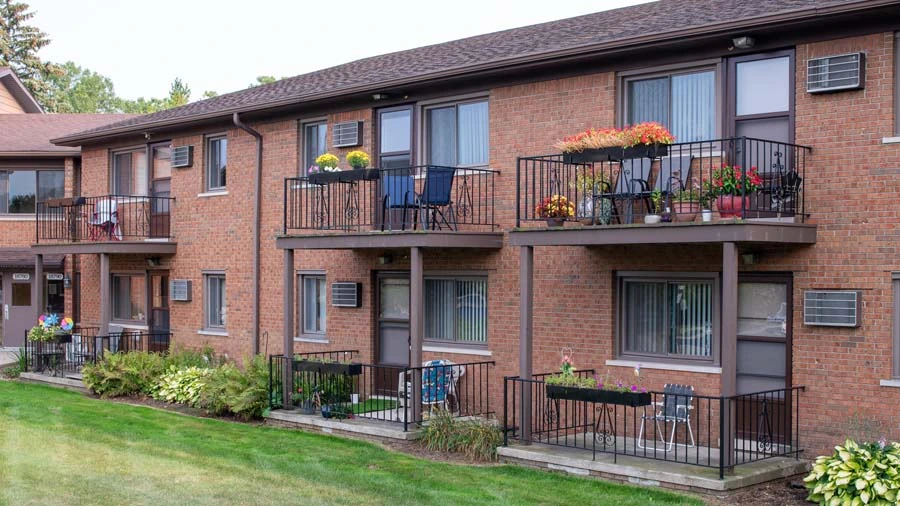 A brick apartment building with balconies and a green lawn.