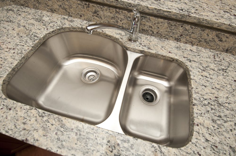 A dual-basin stainless steel kitchen sink set in a granite countertop.